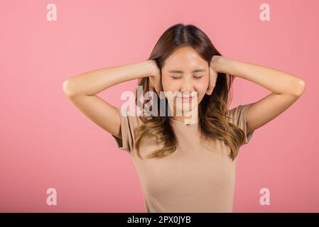 Ritratto asiatico bella giovane donna hanno orecchie strette con mani palme e occhi stretti, studio shot isolato su sfondo rosa, Thai femmina orecchio di copertura Foto Stock