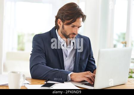 La concentrazione e la determinazione ottengono buoni risultati. Un bell'uomo d'affari che lavora duro sul suo laptop. Foto Stock