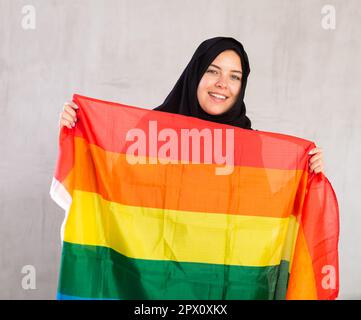 Felice giovane donna vestita con abiti tradizionali islamici con bandiera arcobaleno Foto Stock