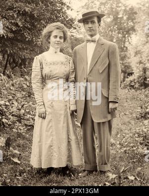 1890S 1900S RITRATTO DI GIOVANE UOMO E DONNA VESTITI ALLA MODA IN PIEDI INSIEME SORRIDENDO GUARDANDO LA FOTOCAMERA - O3993 HAR001 HARS COMPIACIUTA GIOIA LIFESTYLE FEMMINE SPOSATO SPOSO RURALE MARITI HOME VITA COPIA SPAZIO AMICIZIA FULL-LENGTH SIGNORE PERSONE FANTASIA MASCHI B&W PARTNER OCCHIO CONTATTO TUTA E CRAVATTA FELICITÀ STRANI STILI ALLEGRI GIRATA DEL 20TH ° SECOLO E SORRISI CONNESSIONE FASHIONABLY GIOIOSO ELEGANTE CRAVATTA FIOCCO MODA SPOSI NOVELLI MID-ADULTI FIANCO A FIANCO SPOSE GIOVANE ADULTO UOMO NERO E BIANCO CAUCASICO ETNIA HAR001 VECCHIO STILE Foto Stock