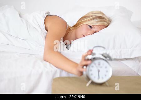 Non può essere che ora già... Una giovane donna che mette la sua sveglia fuori al mattino. Foto Stock