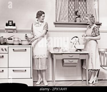 1930S DUE DONNE CHE PARLANO SORRIDENDO MENTRE IN CUCINA UNA PENTOLA DI AGITAZIONE SULLA STUFA ALTRI INGREDIENTI DI AGGIUNGERE AL MISCELATORE ELETTRICO - H5842 HAR001 HARS COMUNICAZIONE BIONDA AMICO GIOVANE ADULTO LAVORO DI SQUADRA PIACERE GIOIA LIFESTYLE CHORES FEMMINE STUDIO SHOT MIXER HOME LIFE COPY SPAZIO AMICIZIA FULL-LENGTH LADIES PERSONE INGREDIENTI FIDUCIA GREMBIULI B&W BRUNETTE ABITI FELICITÀ ALLEGRO CHORE STILI MESCOLANDO ECCITAZIONE AGGIUNGERE SORRISI COMPITI AMICHEVOLE GIOIOSO ELEGANTE SOSTEGNO COOPERAZIONE MODA FUMA COMPITO TOGETHERNESS GIOVANE DONNA ADULTA BIANCO E NERO ETNICITÀ CAUCASICA PREPARAZIONE ALIMENTARE HAR001 TACCHI ALTI Foto Stock