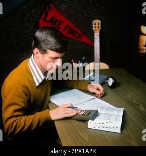 1970S STUDENTE UNIVERSITARIO MASCHILE CHE STUDIA ALLA SCRIVANIA UTILIZZANDO IL LIBRO DI RIFERIMENTO CALCOLATRICE PRENDERE APPUNTI DORMITORIO CAMERA CHITARRA PENNANT IN BACKGROUND - KS14368 BAN001 HARS INFORMAZIONI LIFESTYLE HOME VITA COPIA SPAZIO MEZZA LUNGHEZZA PERSONE PREMUROSI MASCHI ADOLESCENTE RAGAZZO DORMITORIO OBIETTIVI SCUOLE UNIVERSITÀ DI RIFERIMENTO HIGH SCHOOL PENNANT USANDO LE SCUOLE SUPERIORI ISTRUZIONE SUPERIORE COLLEGE ADOLESCENTI SOLENNE FOCALIZZATO CRESCITA INTENSA GIOVANI ADULTO GIOVANE UOMO ATTENTO CAUCASICO ETNIA INTENTO SERIO VECCHIO STILE Foto Stock