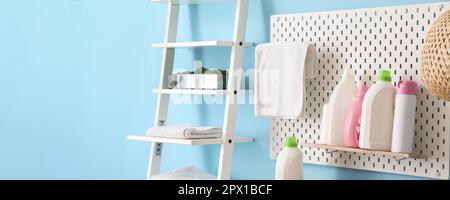 Pegboard con bottiglie di detersivi e rack con asciugamani vicino a parete blu in lavanderia Foto Stock