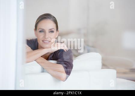 Perso nel pensiero. Una giovane donna che guarda fuori da una finestra mentre si siede su un divano. Foto Stock