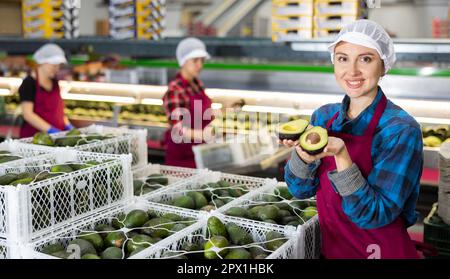 Donna sorridente in magazzino di smistamento frutta con avocado affettato Foto Stock