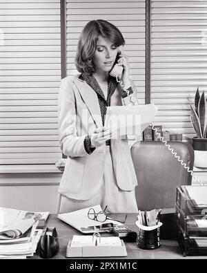 1970S DONNA BUSINESS EXECUTIVE IN PIEDI ALLA SCRIVANIA UFFICIO PARLARE AL TELEFONO LEGGERE DOCUMENTO - O4362 HAR001 HARS STUDIO SHOT COMUNICAZIONE MANAGER COPY SPAZIO METÀ LUNGHEZZA SIGNORE PERSONE PROFESSIONE FIDUCIA DIRIGENTI B&W BUSINESSWOMAN OBIETTIVI ABILITÀ PROFESSIONE ABILITÀ COMPETENZE DOCUMENTO SERVIZIO CLIENTI RETE CARRIERE LEADERSHIP OPPORTUNITÀ OCCUPAZIONI TELEFONI BUSINESS TUTA BOSS CONNESSIONE TELEFONI ELEGANTE DONNE D'AFFARI COOPERAZIONE MANAGER MID-ADULT DONNA MID-ADULT VENEZIANA CIECHI NERO E. ETNIA CAUCASICA BIANCA HAR001 VECCHIO STILE Foto Stock