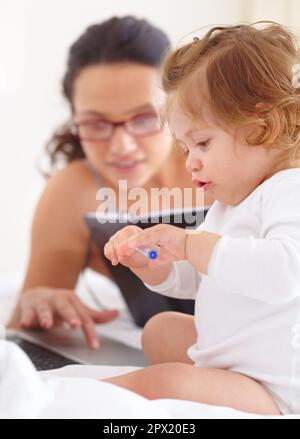 Tenerla occupata mentre cerca di lavorare. Una bambina seduta accanto alla madre e che gioca con una penna a sfera. Foto Stock