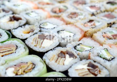 Primo piano di un sacco di sushi roll con diversi ripieni. Macrofo di cucina classica giapponese cotta. Immagine di sfondo Foto Stock