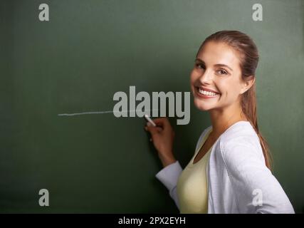 Pronti ad arricchire le giovani menti. Un bel giovane insegnante che scrive su una lavagna mentre sorride alla macchina fotografica. Foto Stock