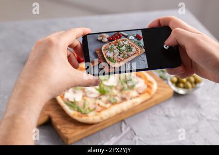 Lo chef scatta foto della pizza italiana con prosciutto di parma su smartphone. Fotografare il concetto di cibo e di social network Foto Stock