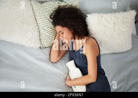Respirare attraverso il dolore. una giovane donna attraente che soffre di crampi d'epoca mentre sdraiata a letto con una bottiglia d'acqua calda Foto Stock