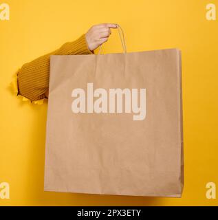 Donna che tiene in mano marrone vuoto sacco di carta da asporto su sfondo giallo. Modello di imballaggio. Servizio di consegna Foto Stock