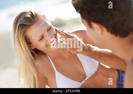 Divertimento con la crema solare. Una giovane coppia che applica crema solare in spiaggia. Foto Stock