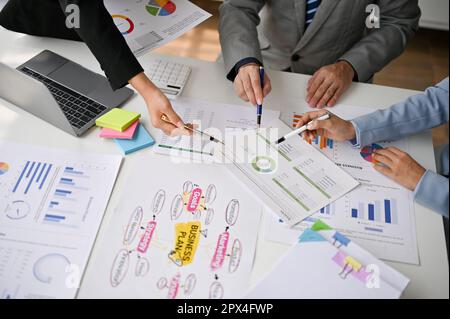 Vista superiore di un professionista businessspeople stanno puntando la loro penna ad un giornale, discutendo, brainstorming e votando su un programma. Foto Stock