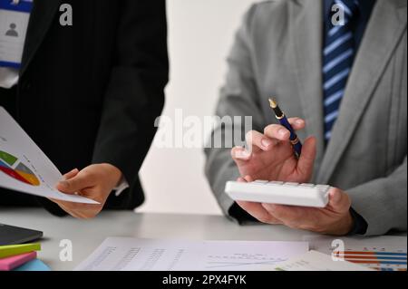 Immagine ritagliata di un uomo d'affari professionale utilizzando una calcolatrice e parlando con il suo assistente durante la riunione. Foto Stock