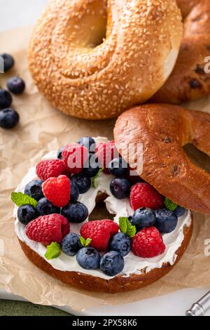 Bagel appena sfornati fatti in casa su carta da pergamena pronta da mangiare, bagel di uva passa alla cannella con formaggio cremoso e frutti di bosco freschi Foto Stock