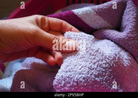 La mano di una donna sente un asciugamano di cotone colorato da un cesto con bucato sporco. Lavanderia selezione e lavaggio. Lavanderia o bagno. Servizio di pulizia Foto Stock