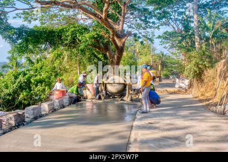 Puerto Galera, Filippine - 22 aprile 2023. Operai filippini che mescolano e versano una lastra di cemento su un progetto di pavimentazione stradale nei pressi del villaggio di Baclayan. Foto Stock