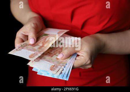 Rubli russi in mani femminili, retribuzione in contanti, stipendio, inflazione o concetto di risparmio. Donna in abito rosso contando valuta di carta della Russia Foto Stock