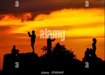 Silhouette di persone sul rock scattare foto e selfie su sfondo arancione cielo Foto Stock