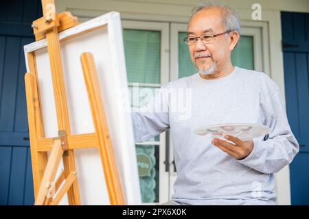 Stile di vita persone anziane sorridono dipingere al suo cavalletto fuori casa, asiatico anziano pittura immagine utilizzando pennello e olio di colore su tela, felice pensir Foto Stock