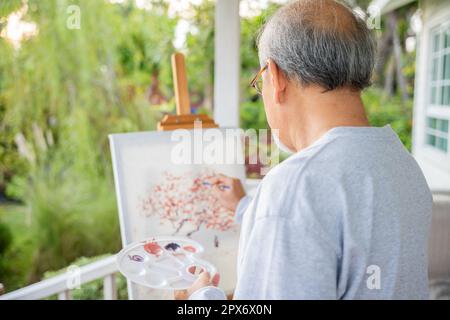 Stile di vita Asiatico anziano pittura di illustrazione dell'immagine dell'uomo usando il colore del pennello e dell'olio sulla tela, la gente anziana sorride vernice al suo cavalletto fuori del nat verde Foto Stock