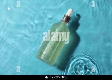 Bottiglia di olio idrofilo in acqua su sfondo azzurro, vista dall'alto Foto Stock