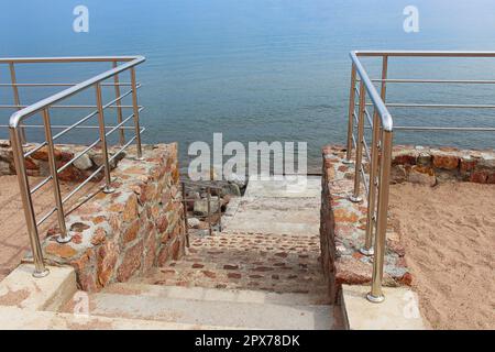 Scala in pietra di marmo direttamente nel mare blu con corrimano e sabbia. Linea costiera. Estate. Spazio di copia Foto Stock