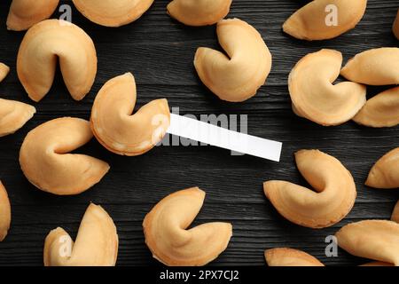 Biscotti gustosi della fortuna con predizioni su tavolo di legno nero, piatto. Spazio per il testo Foto Stock