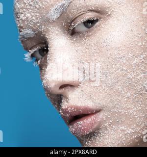 Ritratto di una ragazza con pelle pallida e neve di zucchero sul viso. Arte creativa bellezza moda. Foto scattata in studio su sfondo blu. Foto Stock