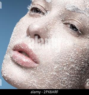 Ritratto di una ragazza con pelle pallida e neve di zucchero sul viso. Arte creativa bellezza moda. Foto scattata in studio su sfondo blu. Foto Stock