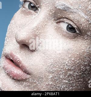 Ritratto di una ragazza con pelle pallida e neve di zucchero sul viso. Arte creativa bellezza moda. Foto scattata in studio su sfondo blu. Foto Stock