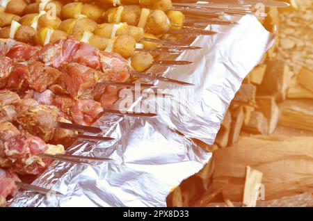 La carne cruda e le patate sono piantati su spiedini di metallo. Il processo di cottura shish kebab. Russo e ucraino cibo camp Foto Stock