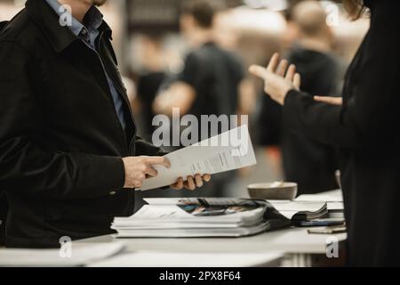 Uomini d'affari che scambiano materiale promozionale e brochure sulla riunione d'affari sulla fiera. Concetto di trattativa parlante di discussione di affari Foto Stock