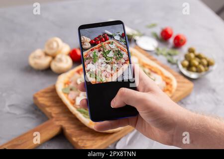 Lo chef scatta foto della pizza italiana con prosciutto di parma su smartphone. Fotografare il concetto di cibo e di social network Foto Stock