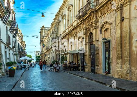 Turisti che camminano lungo la strada principale della città barocca di noto. I palazzi nobiliari riccamente decorati si affacciano sulla strada. Noto, Sicilia Foto Stock