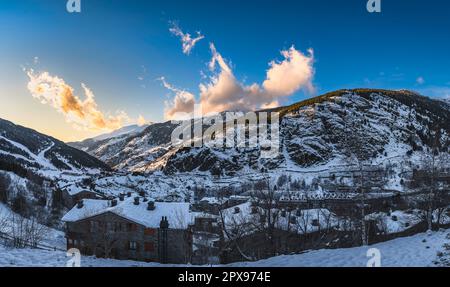 Vista panoramica sul villaggio di El Tarter con nuvole e montagne illuminate dal tramonto e valle in ombra profonda. Sci vacanze invernali, Andorra, Pirenei Foto Stock