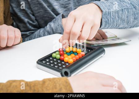 Foto ritagliata di due ragazzi amici seduti al tavolo in cucina a casa, tenendo istruzioni, giocando colorato puzzle 3D classico gioco piramide, mettendo b Foto Stock