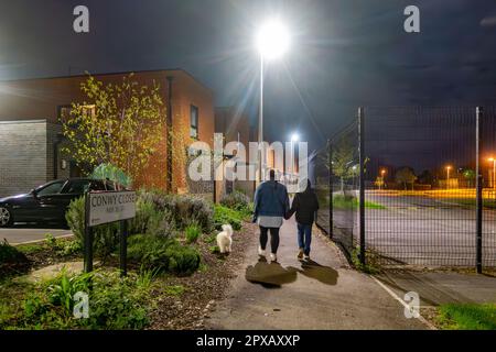 Una famiglia cammina il loro cane nel tardo buio di sera, camminando lungo un sentiero Foto Stock