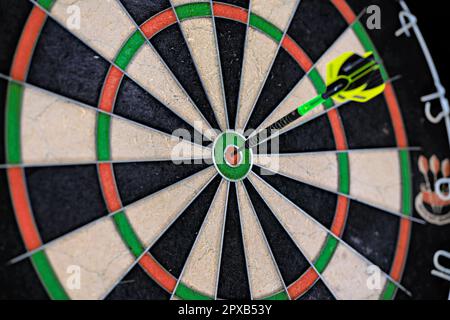 Singola freccetta nera e verde bloccata nel bullseye di una freccetta. Primo piano di una tavola da disegno. Foto Stock