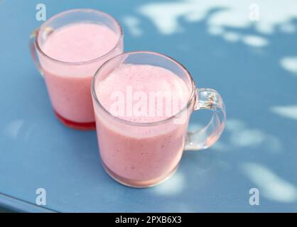 Due frullati di frutta rosa in bicchieri di vetro si trovano su un tavolo in un bar sulla strada Foto Stock