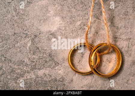 Anelli di nozze appesi su corda su sfondo di pietra grigia. Amore e matrimonio. Spazio di copia. Foto Stock