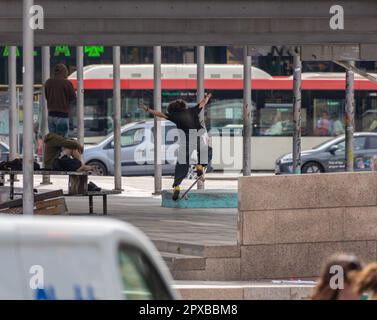 Giovane skater urbano alternativo in azione divertente saltando e eseguendo pose e trucchi sullo skateboard in un parco di strada, con i suoi amici vestiti in alter Foto Stock