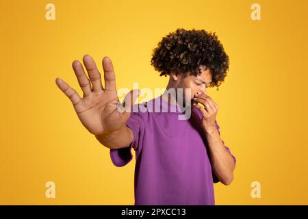Infelice uomo afroamericano in t-shirt viola che copre il naso, facendo segno di stop Foto Stock