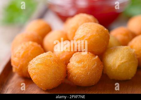 Patate della duchessa o crocchette fresche al forno su tavola di legno, ketchup sul retro (profondità di campo molto bassa, fuoco sulle palle di patate nella f Foto Stock