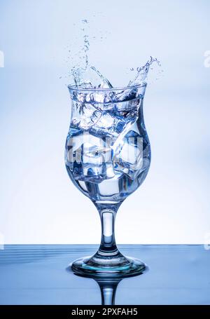 L'immagine di versare acqua potabile, in un vetro rotto, che fa sentire rinfrescato su sfondo bianco sfocato, spruzzi d'acqua, acqua frizzante, Foto Stock