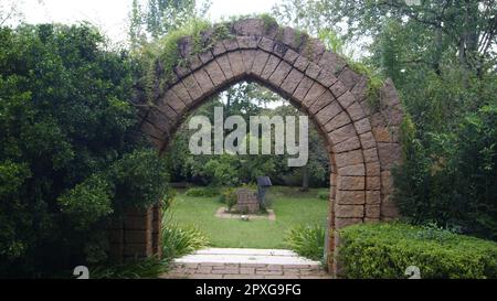 Portale con architettura in pietra con vegetazione in alto e sui lati del giardino inferiore con prato e architettura in pietra e ferro. Foto Stock