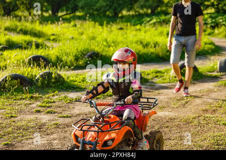 Padre e figlia giocano sulla strada all'ora del giorno. Guidano in quad nel parco. Persone che si divertono sulla natura. Concetto di amichevole Foto Stock