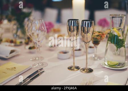 Un tavolo con diversi bicchieri, piatti, candele e fiori in vasetti di vetro, che presentano un'atmosfera festosa Foto Stock